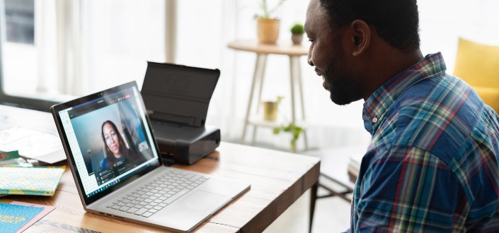 man in blue shirt talking to someone on his laptop