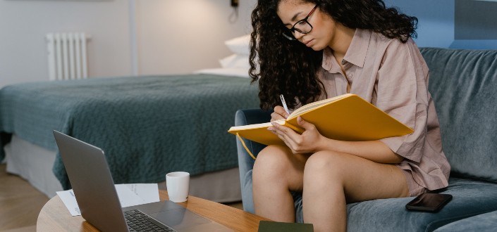 Woman Writing in a Notebook While Sitting on a Couch