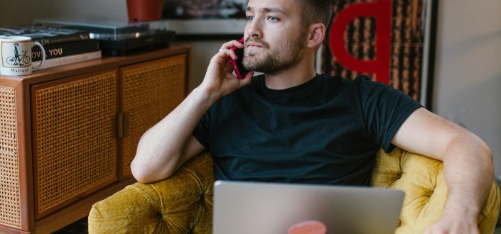 A man sitting on a yellow couch while taking a phone call