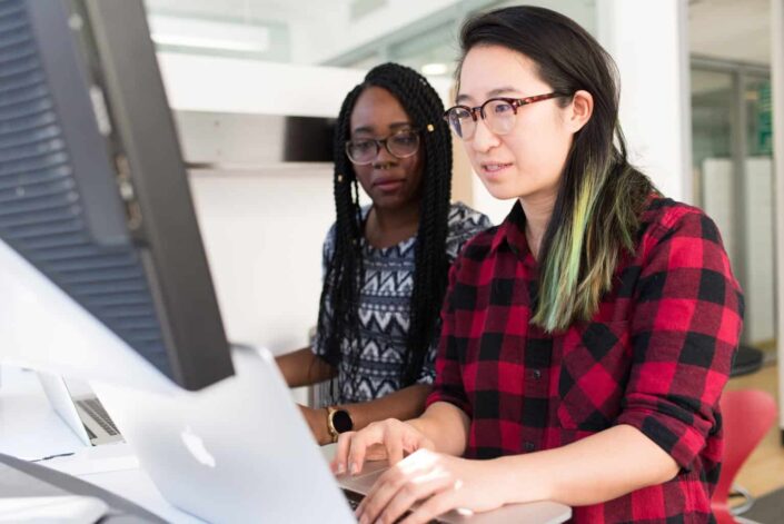 two women using macbook