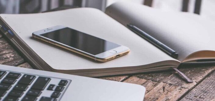 Gold Iphone 7 on Top of Book Beside Macbook