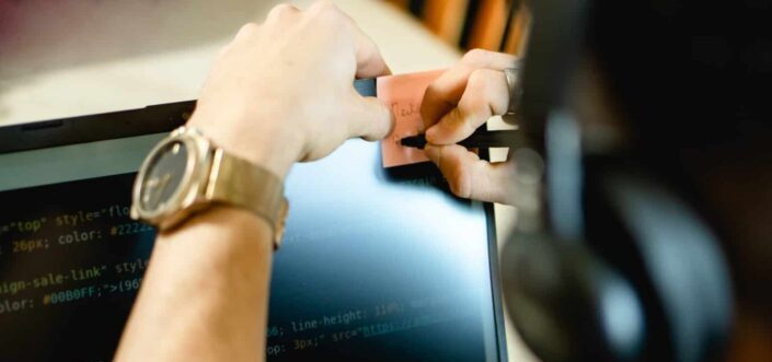 Person Writing on Sticky Note On Laptop